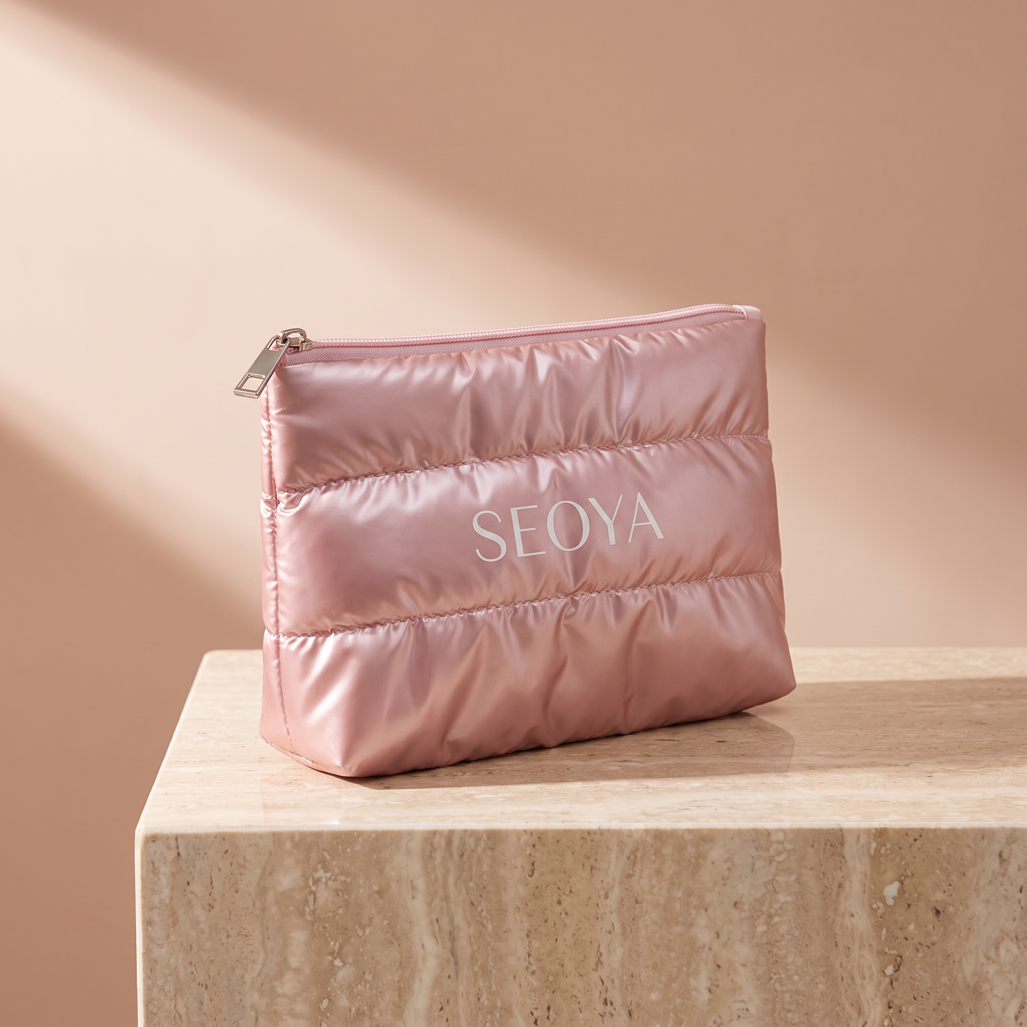 Trousse matelassée SEOYA rose nacré avec zip métal, posée sur un socle en travertin
